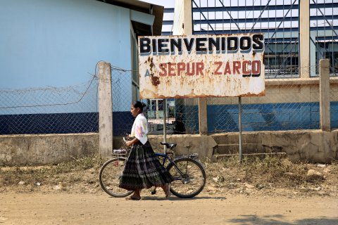 A Q'eqchi' woman with a bicycle walks down the unpaved main road through Sepur Zarco.